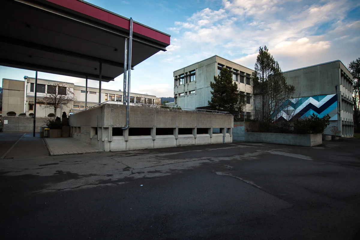 Die Schulanlage Walenbach ist in die Jahre gekommen. Eine Sanierung ist laut Sandra Elliscasis dringend notwendig. Man sieht eine alte Schulanlage mit einem geteerten Platz.